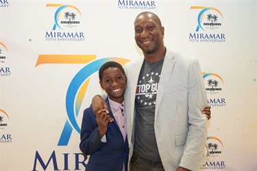 A man and a child hugging in front of the Miramar 70th Anniversary Step and Repeat
